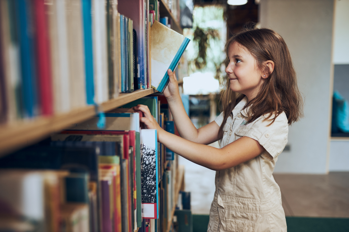 A kid picking out a book off a shelf.
