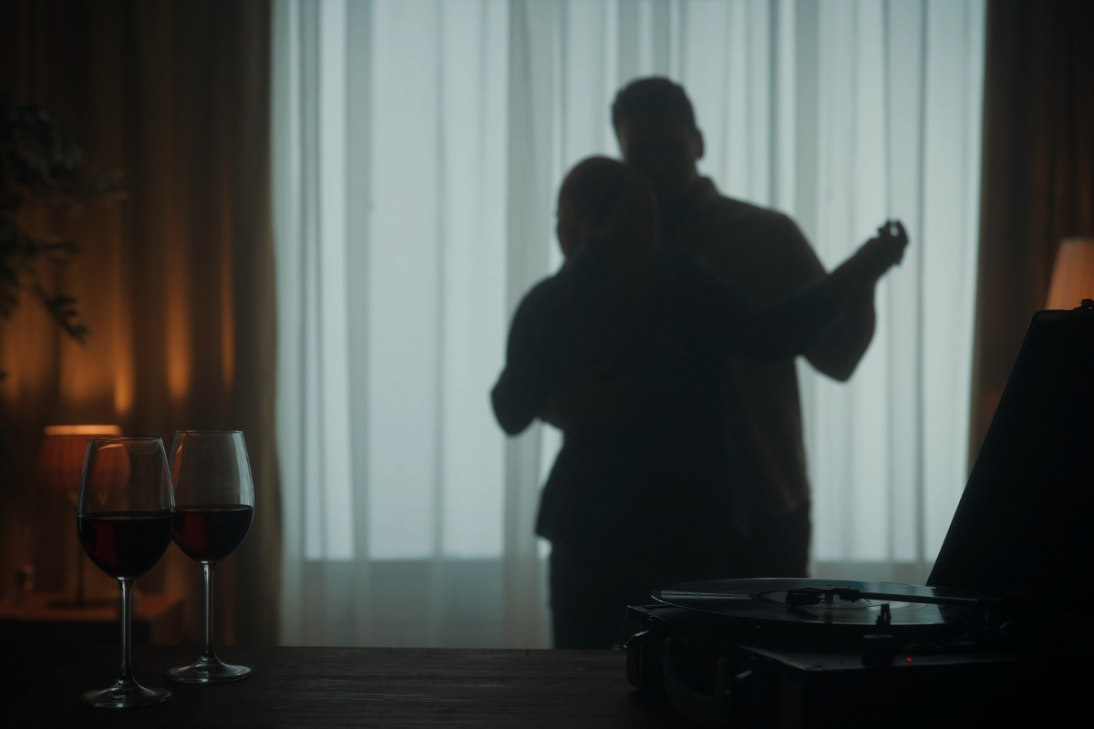 A couple slow dancing in dim lighting with wine and music.