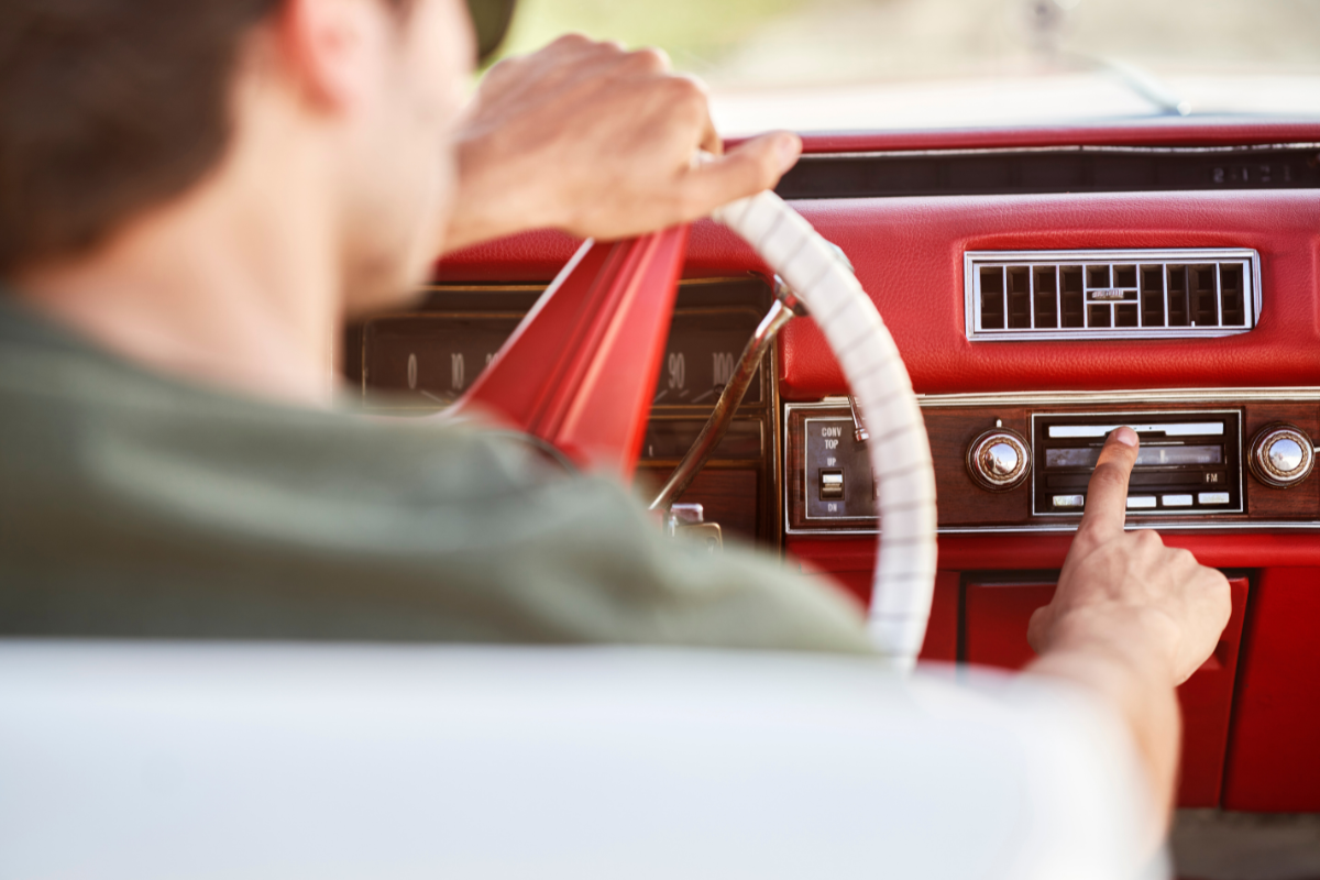 A man driving an old car playing a song on the radio.