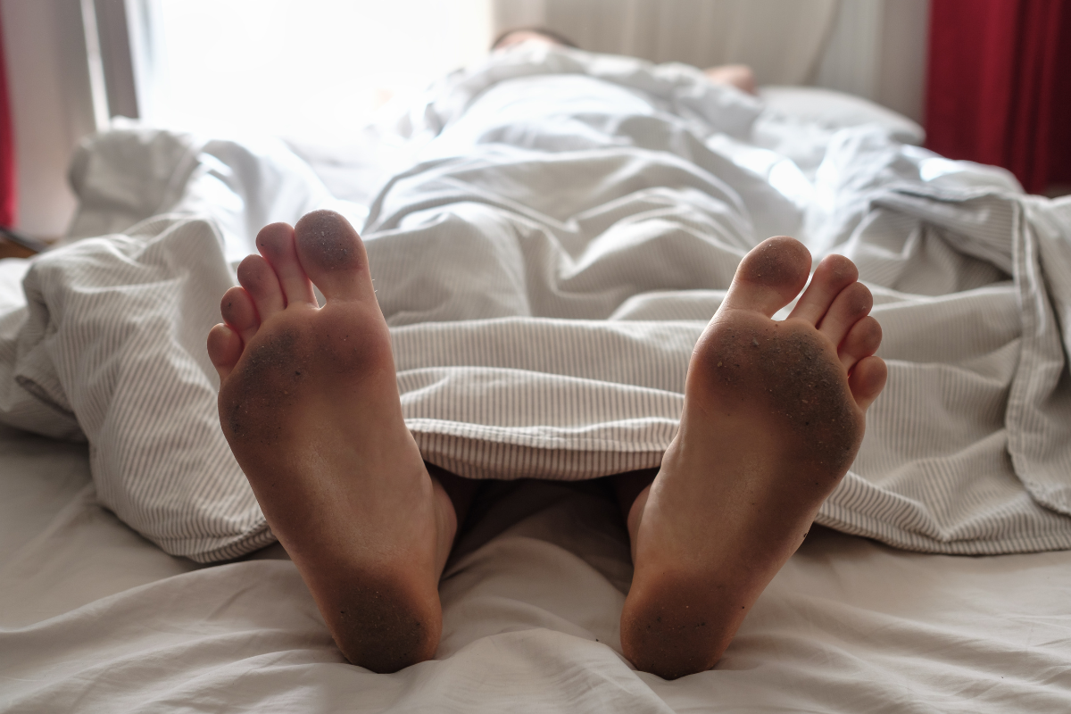 Dirty feet peaking out of bed sheets.