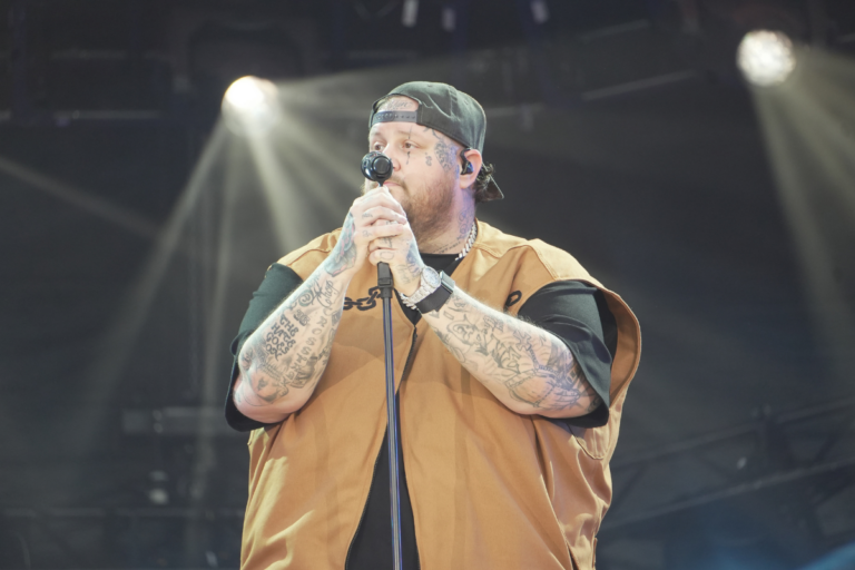 Jellyroll performing live at the Global Citizen Festival on September 28, 2024. The artist is on stage ready to sing, holding both arms with microphones, engaging the audience with his energetic performance.