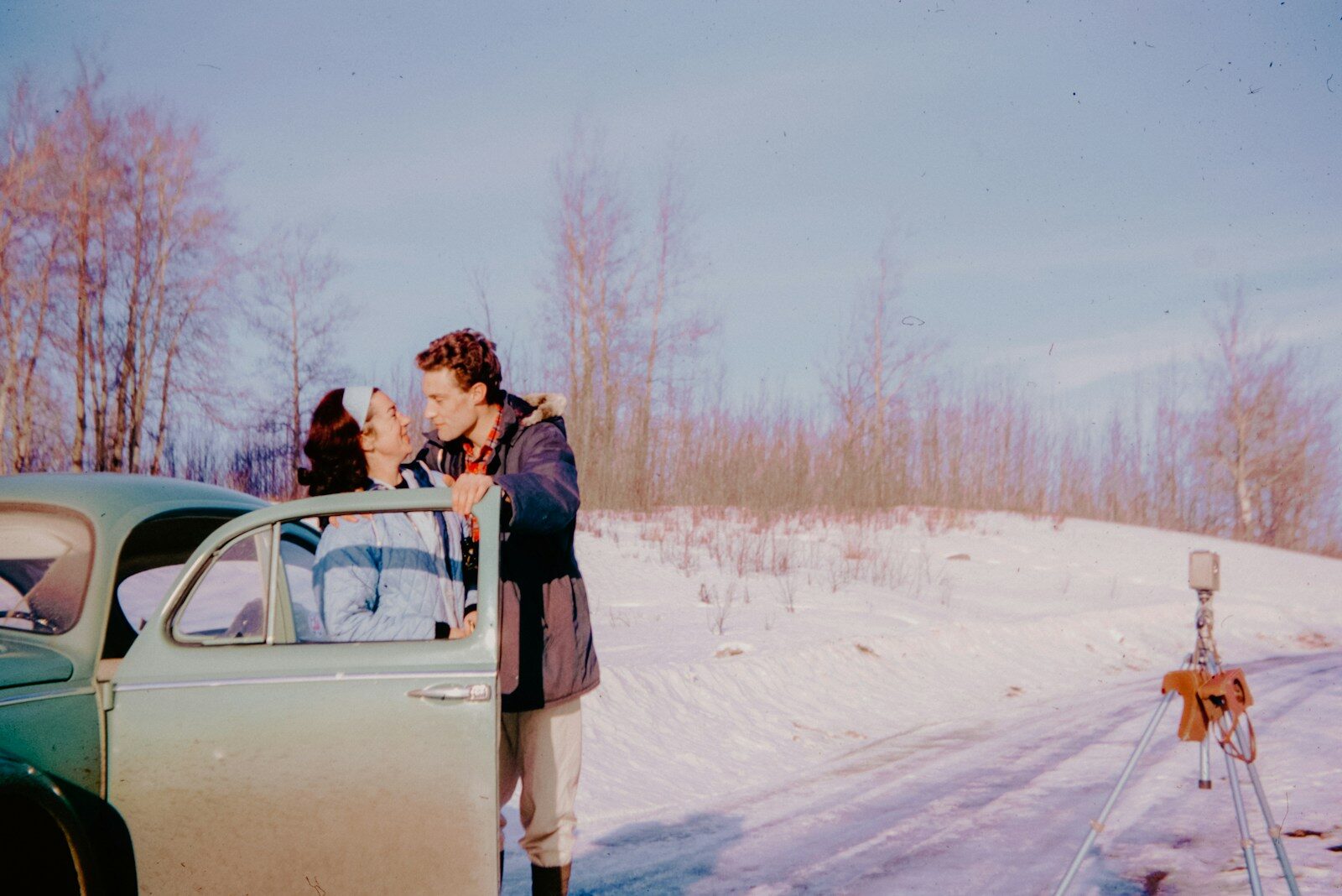 A man and a woman standing next to a car in the snow