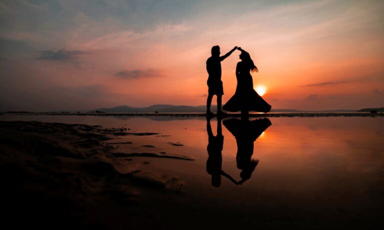 A silhouette of two people dancing on a beach at golden hour