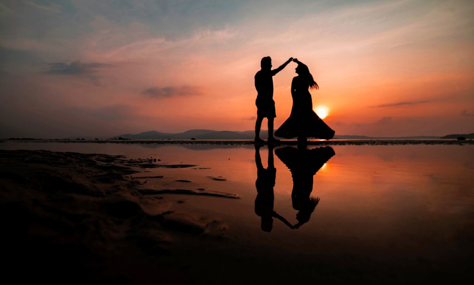 A silhouette of two people dancing on a beach at golden hour